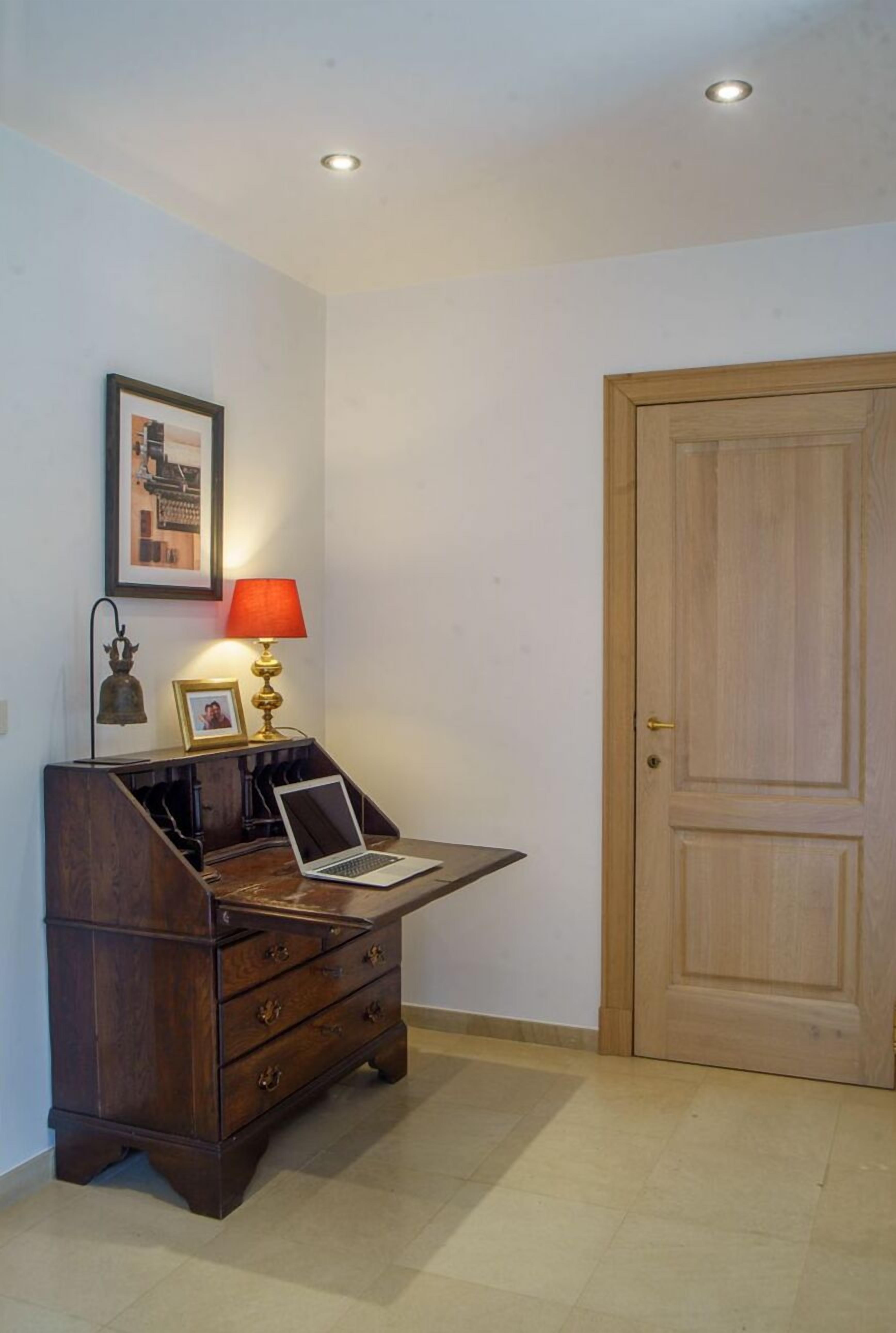 Ein Zimmer mit einem Holztisch, einem Laptop, einer roten Lampe, einem gerahmten Bild und einer Holztür.