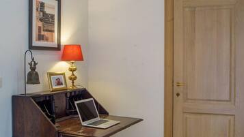 Ein Zimmer mit einem Holztisch, einem Laptop, einer roten Lampe, einem gerahmten Bild und einer Holztür.
