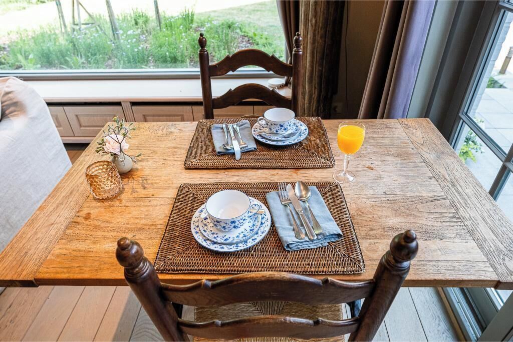 Une table de salle à manger en bois, avec deux jeux d’assiettes bleues et blanches, des couverts en argent et un verre de jus d’orange.