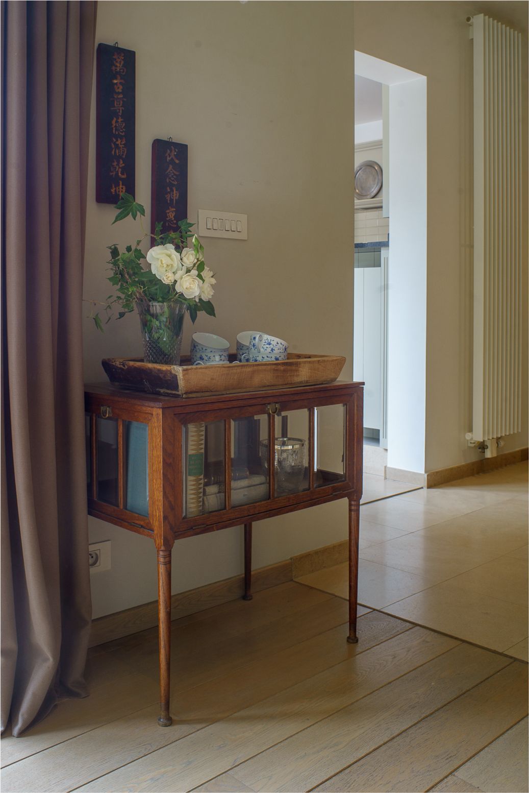 A wooden console table with a vase of white flowers, a tray, and blue patterned cups.