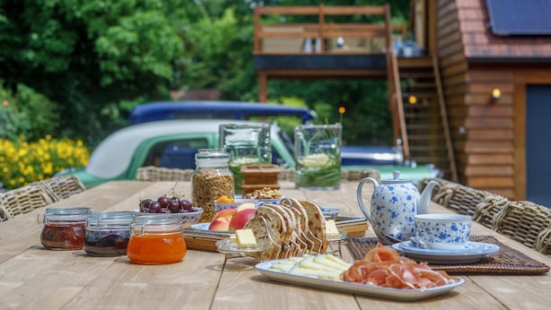 A breakfast table with various food items and a teapot, set outdoors with a wooden structure and greenery in the background. - Villa Magdalena (Eeklo)