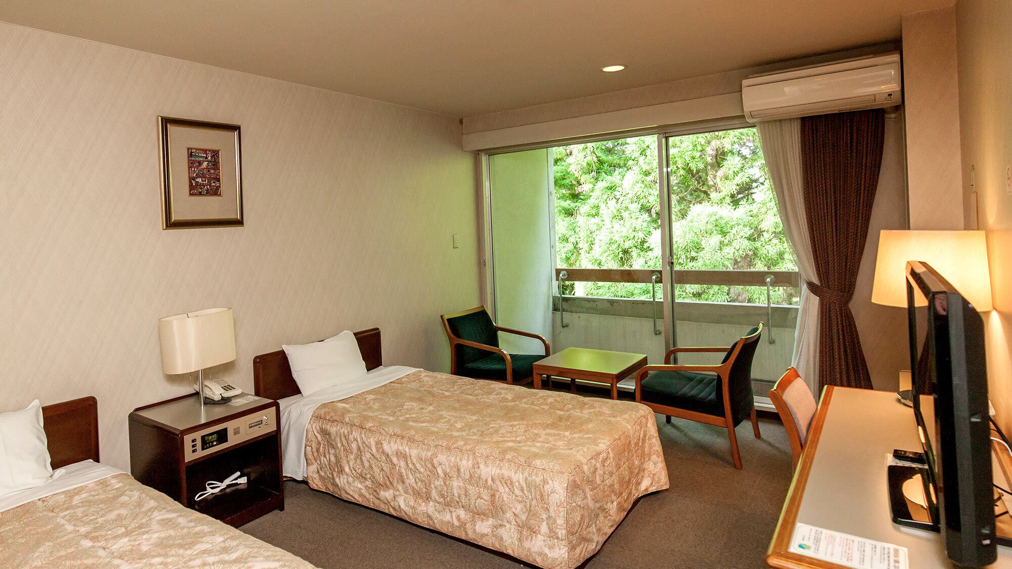 Une chambre d’hôtel avec deux lits, un bureau, une chaise, un téléphone et une fenêtre donnant sur un espace verdoyant.