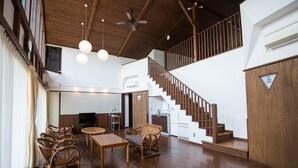 A spacious living area with a wooden floor, a dining table, wicker furniture, a staircase, and a TV in the background. - YMCA International Youth Center TOZANSO (Gotemba)