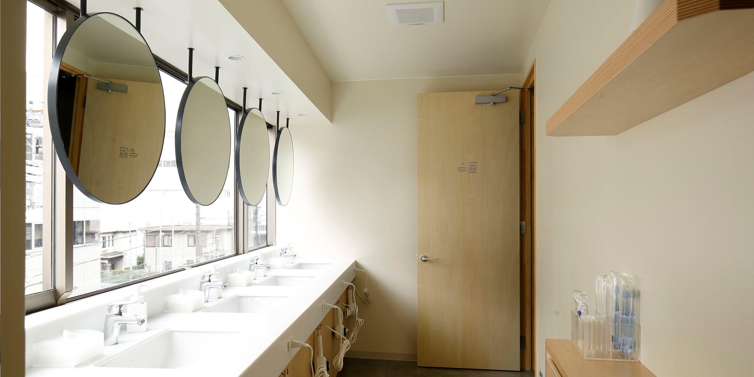 Un baño moderno con tres lavamanos, espejos grandes y una puerta de madera.