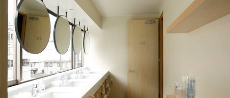 Un baño moderno con tres lavamanos, espejos grandes y una puerta de madera.