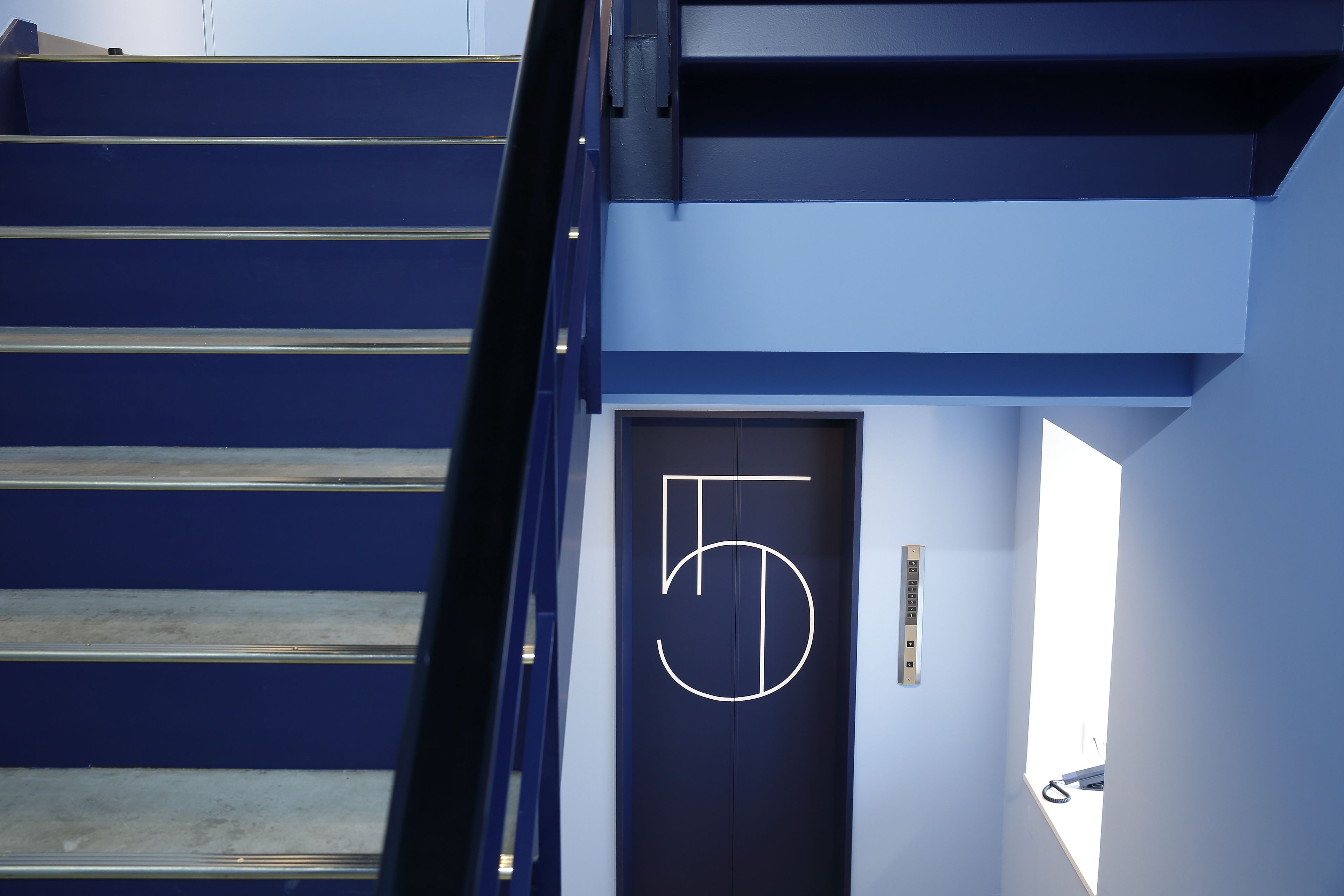 Una escalera con acabado azul oscuro y una puerta con el número 5.