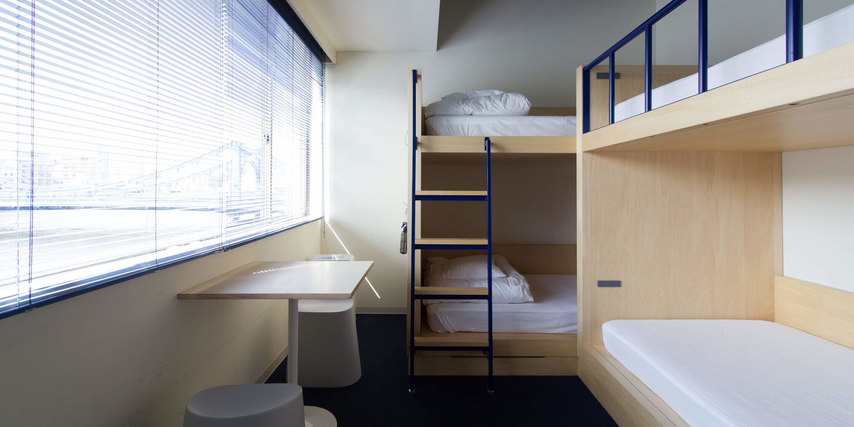 A compact room with bunk beds, a small desk, and a window with blinds.