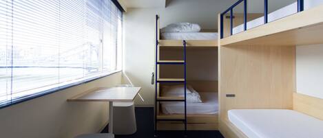 A compact room with bunk beds, a small desk, and a window with blinds.