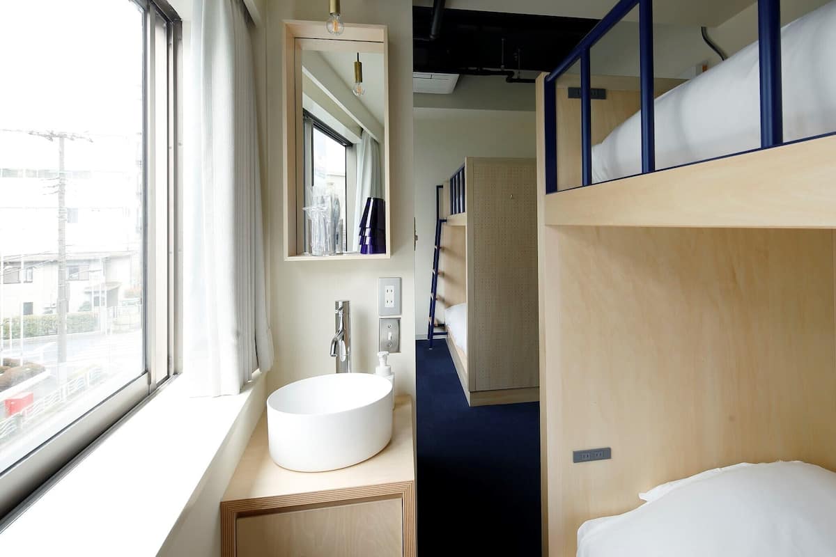 A bunk bed room with a window, sink, mirror, and a small hallway.
