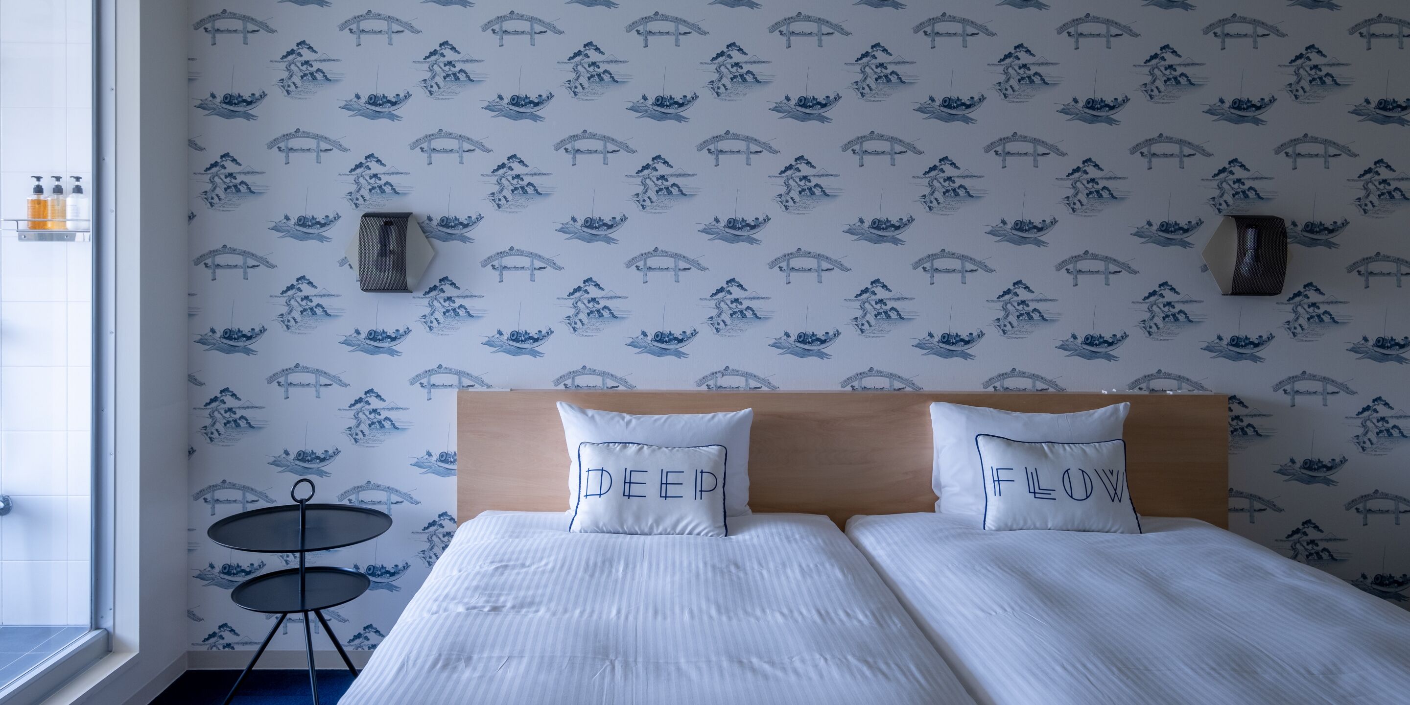 Camera d'albergo con un letto, due cuscini con scritte, un tavolino e una parete decorata.