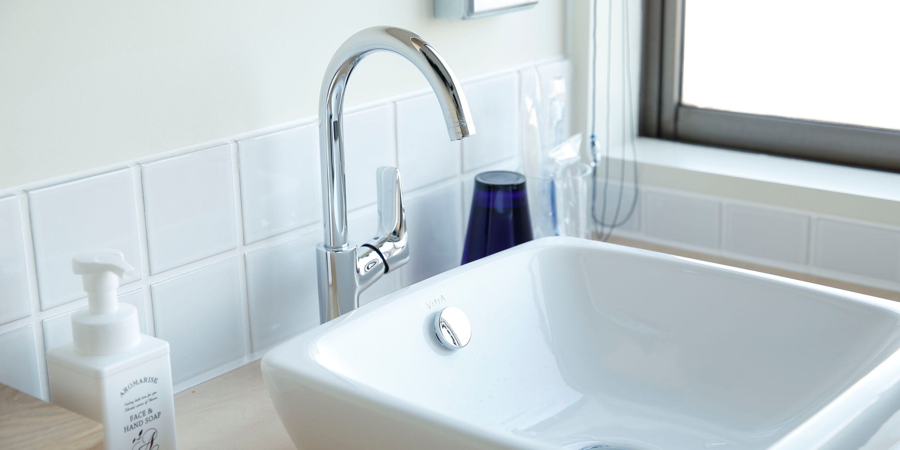 A white bathroom sink with a chrome faucet, a bottle of hand soap, and a blue glass.