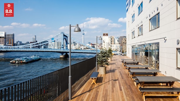 Eine Dachterrasse mit Holztischen und -bänken, mit Blick auf einen Fluss, eine Brücke und Gebäude im Hintergrund.