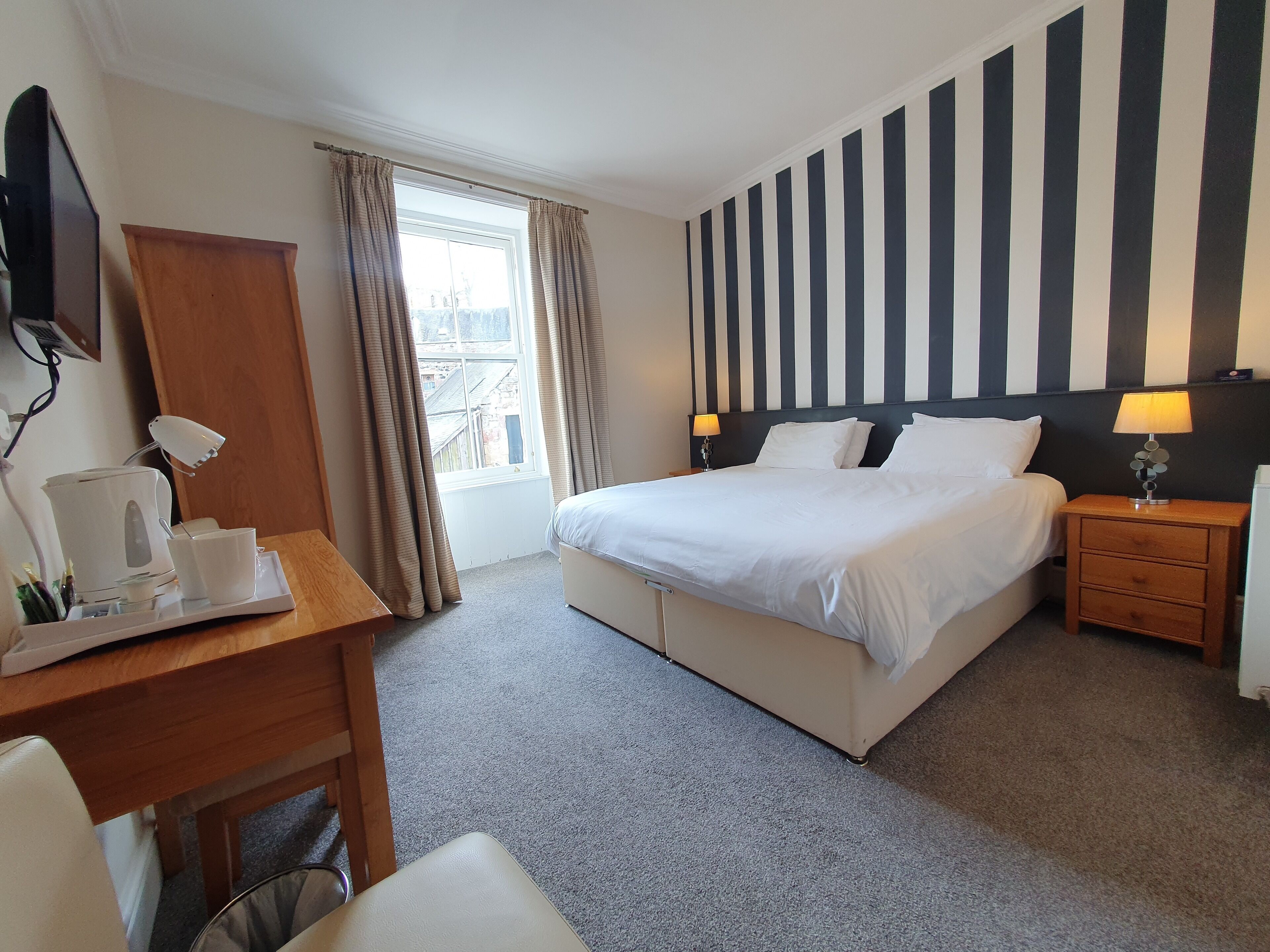 Een hotelkamer met een bed, nachtkastjes, een bureau met koffiezetapparaat en een raam met gordijnen.
