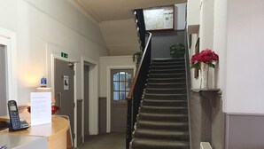 A hotel reception area with a reception desk, a telephone, a welcome sign, a staircase, and a plant. - The Royal Hotel (Jedburgh)
