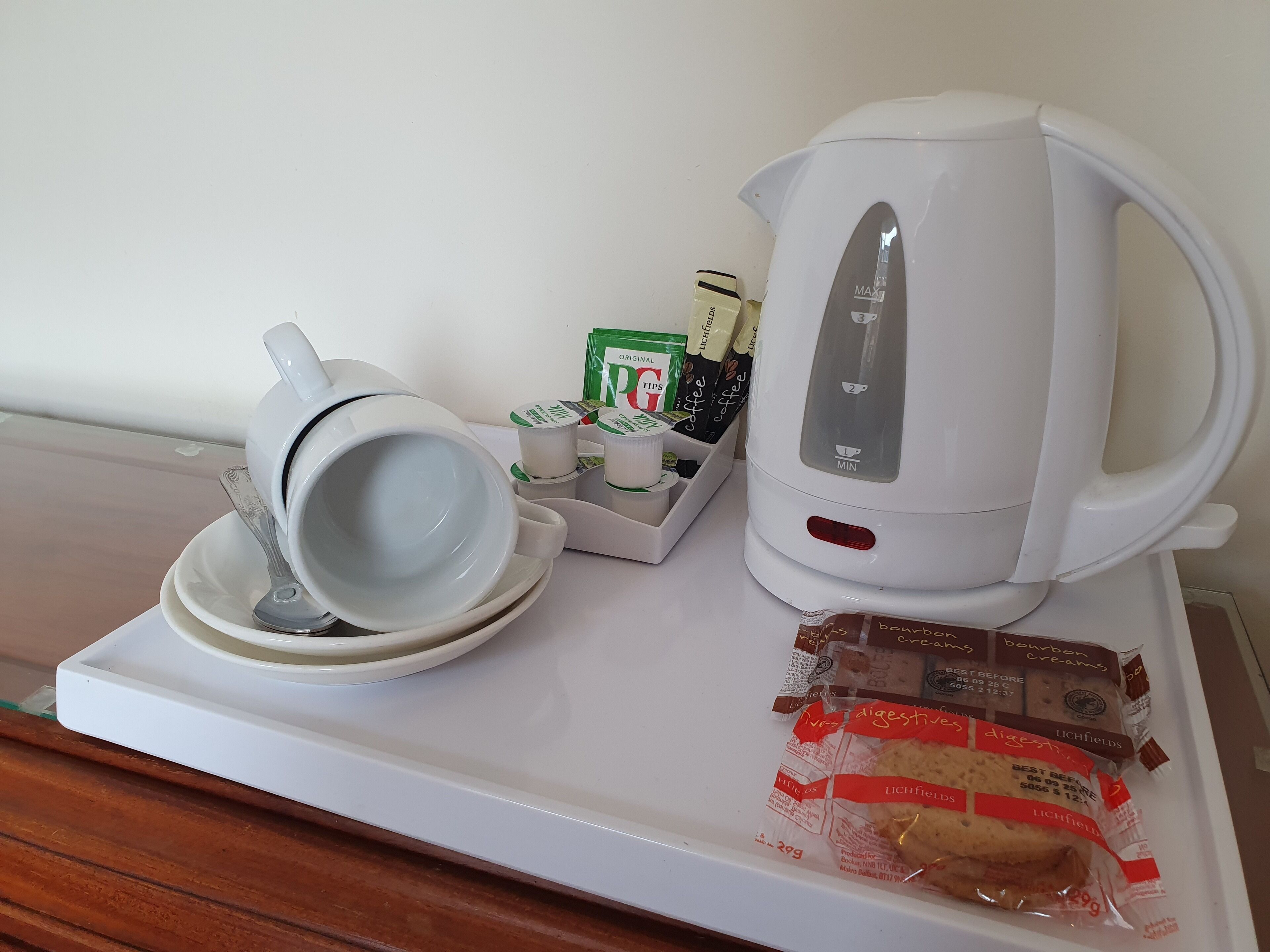 A white tray with a coffee maker, a cup and saucer, a coffee pod holder, and packaged biscuits.