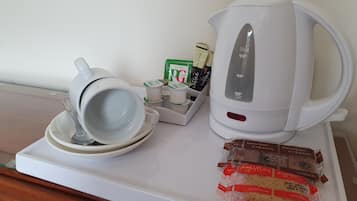 Una bandeja blanca con cafetera, taza y platillo, soporte para cápsulas de café y galletas empaquetadas.