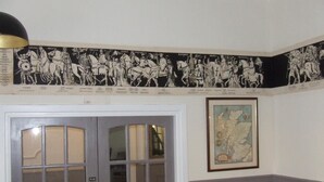 A room with a large window, a door with a push bar, a framed map on the wall, and a black and white mural depicting historical figures. - The Royal Hotel (Jedburgh)