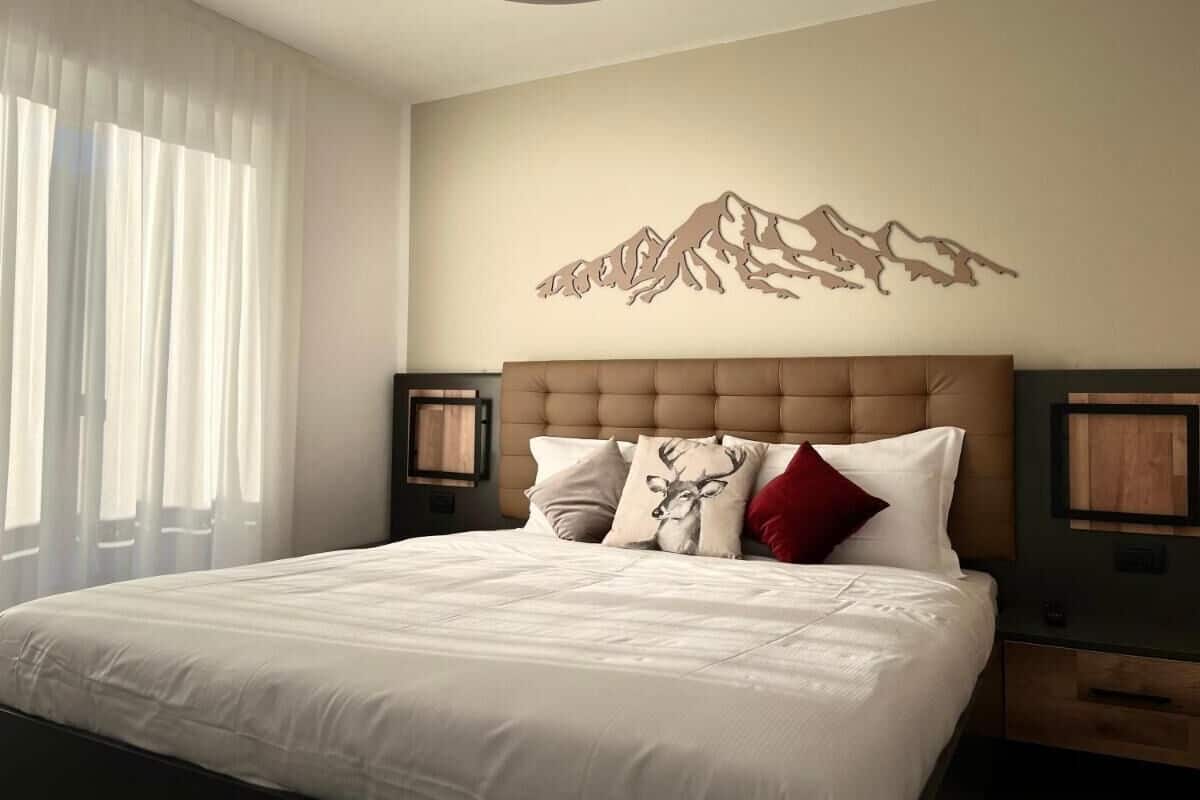 A bedroom with a large bed, a mountain artwork on the wall, and a window with curtains.