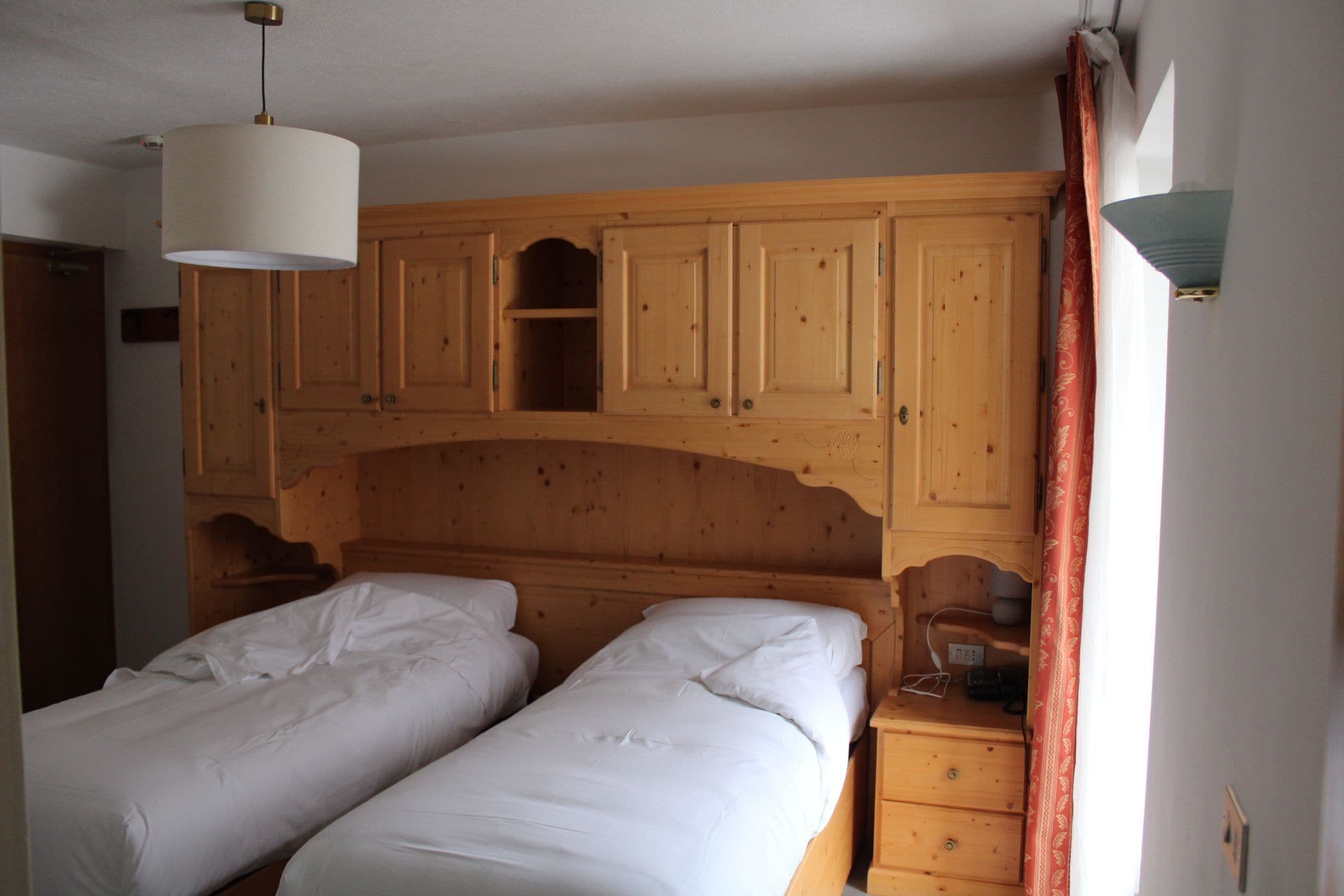 Un dormitorio con dos camas individuales, cabecero de madera y una mesita de noche pequeña con lámpara.