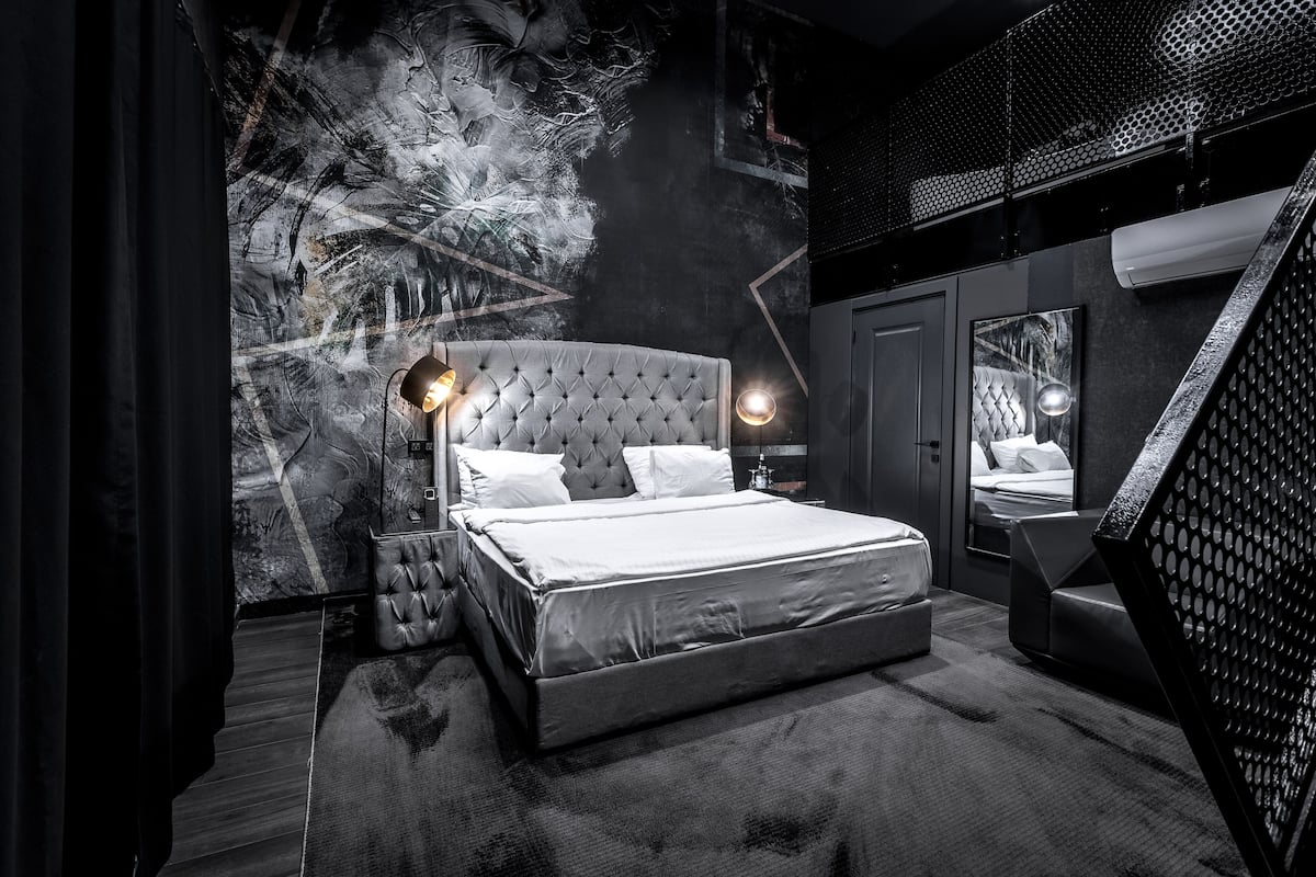 A modern bedroom with a tufted headboard, a large bed, a nightstand, a floor lamp, and a mirror.