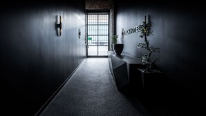 Un hall d’hôtel moderne au design minimaliste, comprenant un comptoir d’accueil, une plante en pot et une grande fenêtre offrant une vue sur l’extérieur.