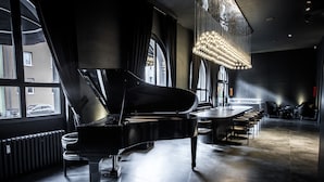 Un piano à queue dans une pièce moderne dotée de grandes fenêtres, d’un lustre et d’un coin bar.