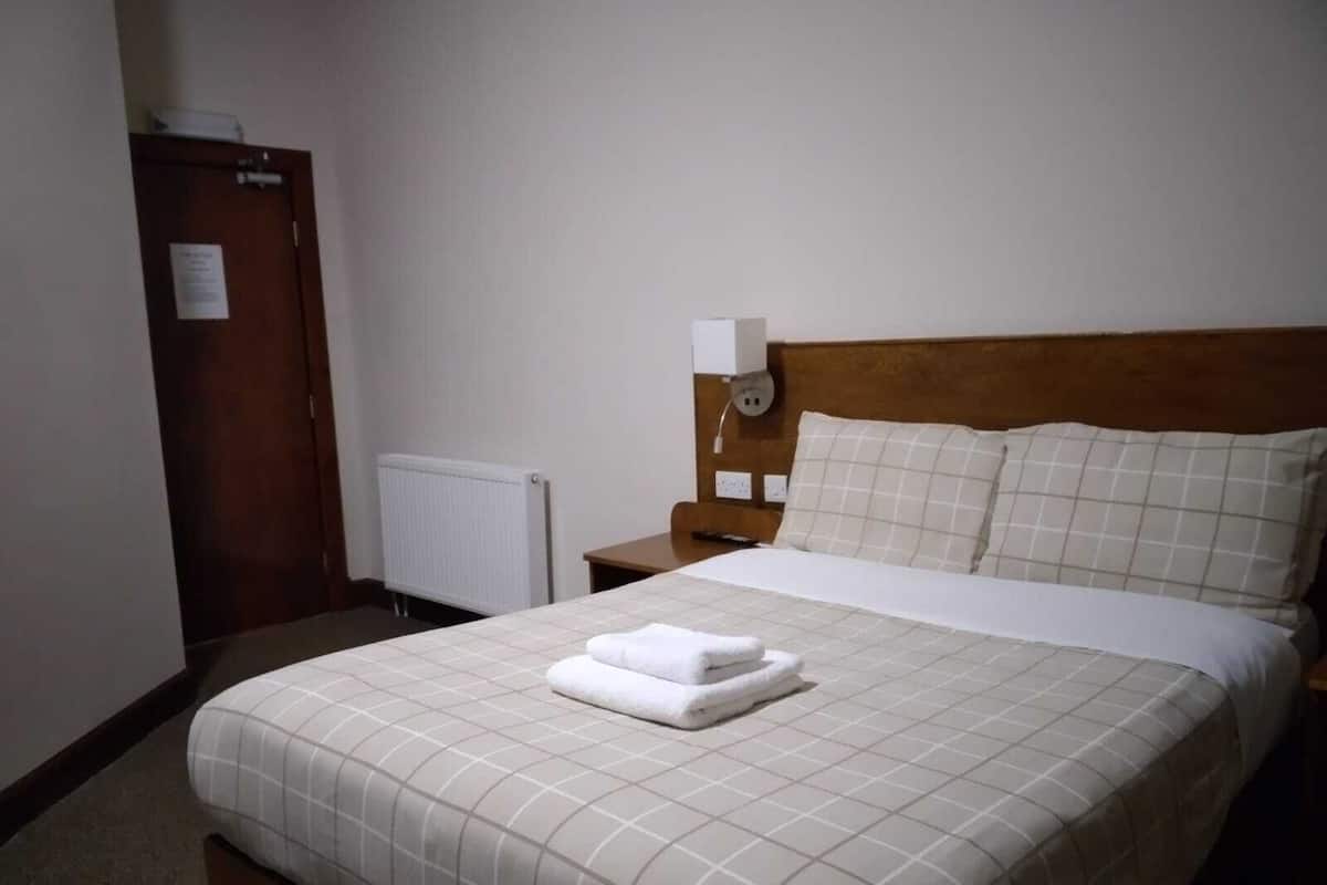 A hotel room with a bed, a nightstand, a wall socket, and a door.