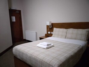Una habitación de hotel con una cama, una mesita de noche, un enchufe y una puerta.