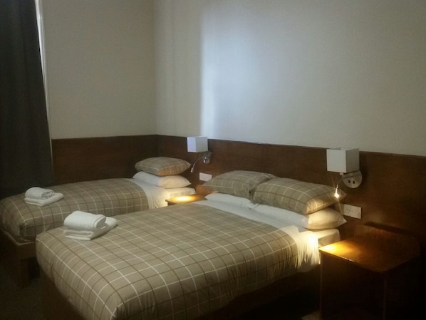A hotel room with two beds, each with a headboard, bedside tables, and lamps.