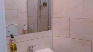 Un baño con lavamanos, espejo y ducha con mampara de vidrio.
