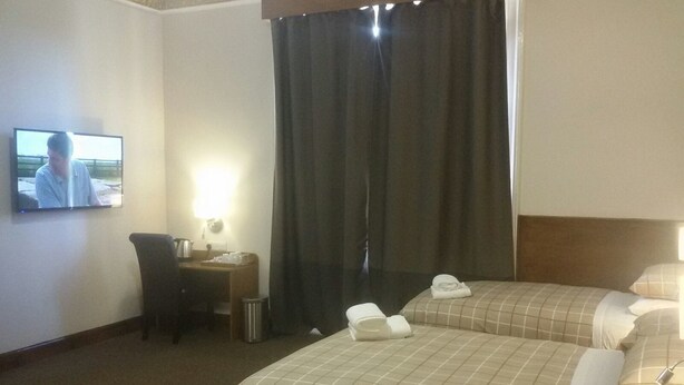 Una habitación de hotel con dos camas, un escritorio, un televisor y una cortina.