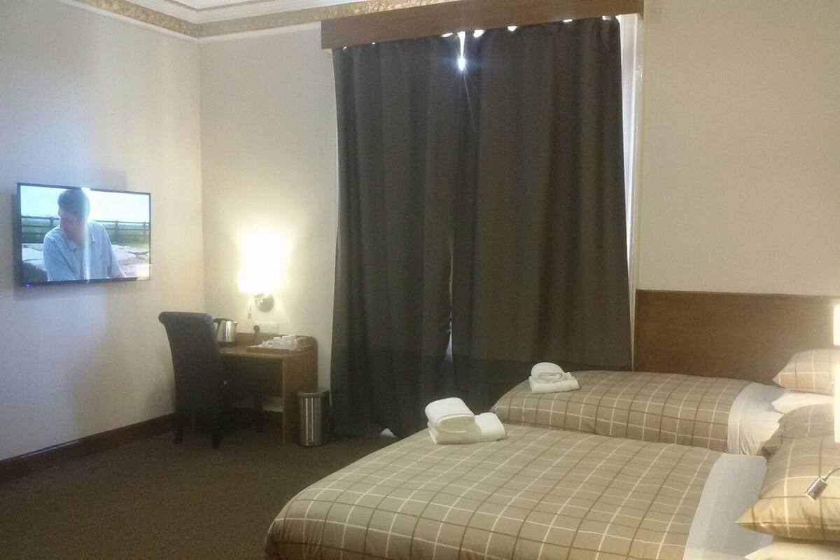 A hotel room with two beds, a desk, a television, and a curtain.