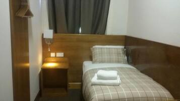 A hotel room with a bed, a nightstand, a lamp, and a window with curtains.