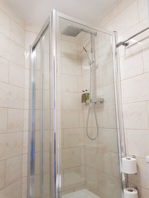 Un box de ducha con paredes de vidrio, un cabezal de ducha de mano y un grifo de pared.