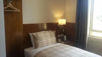 Een hotelkamer met een bed, een bedlamp, een houten hoofdeinde en een raam met gordijnen.