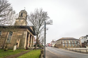 A historic building with a clock tower, large windows, and a paved street in front.
