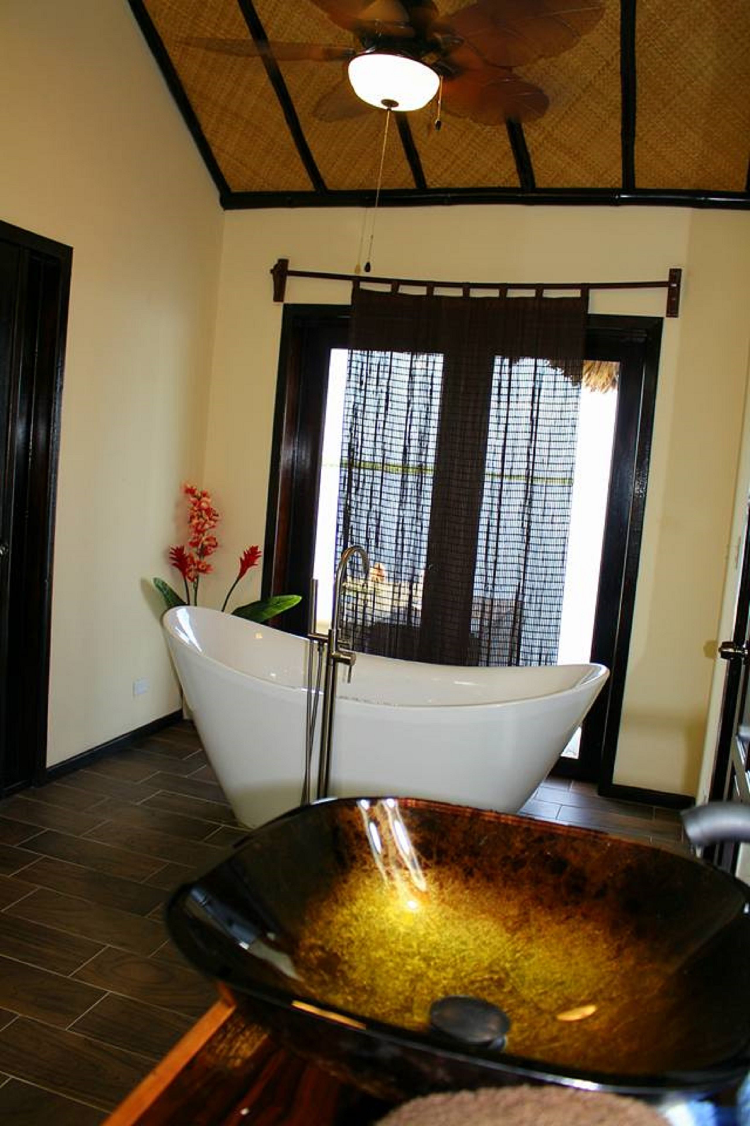 A bathroom with a freestanding bathtub, a large glass bowl sink, and a ceiling fan.
