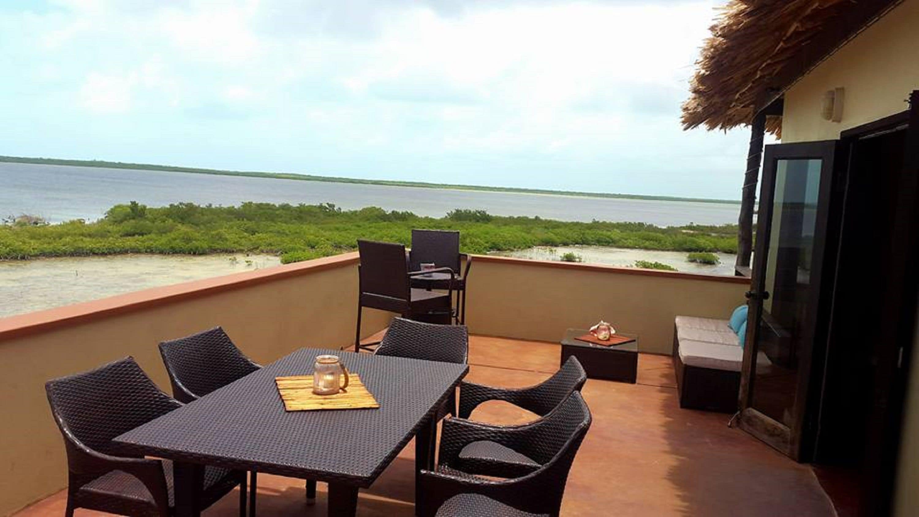 Un balcone con tavolo e sedie, un piccolo tavolino con una candela e vista sul mare e sul verde.