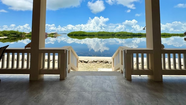A covered outdoor area with a view of a calm lake and a small island, featuring a tiled floor and wooden railings. - Lina Point Belize Overwater Resort (San Pedro)