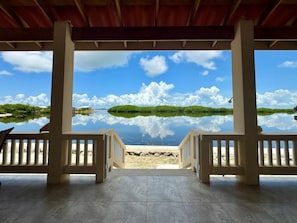 A covered outdoor area with a view of a calm lake and a small island, featuring a tiled floor and wooden railings.