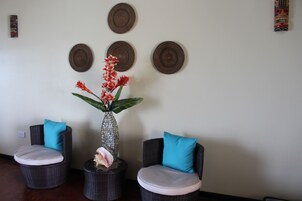Una habitación con dos sillas de mimbre, cada una con un cojín, y un florero con flores sobre una mesita.