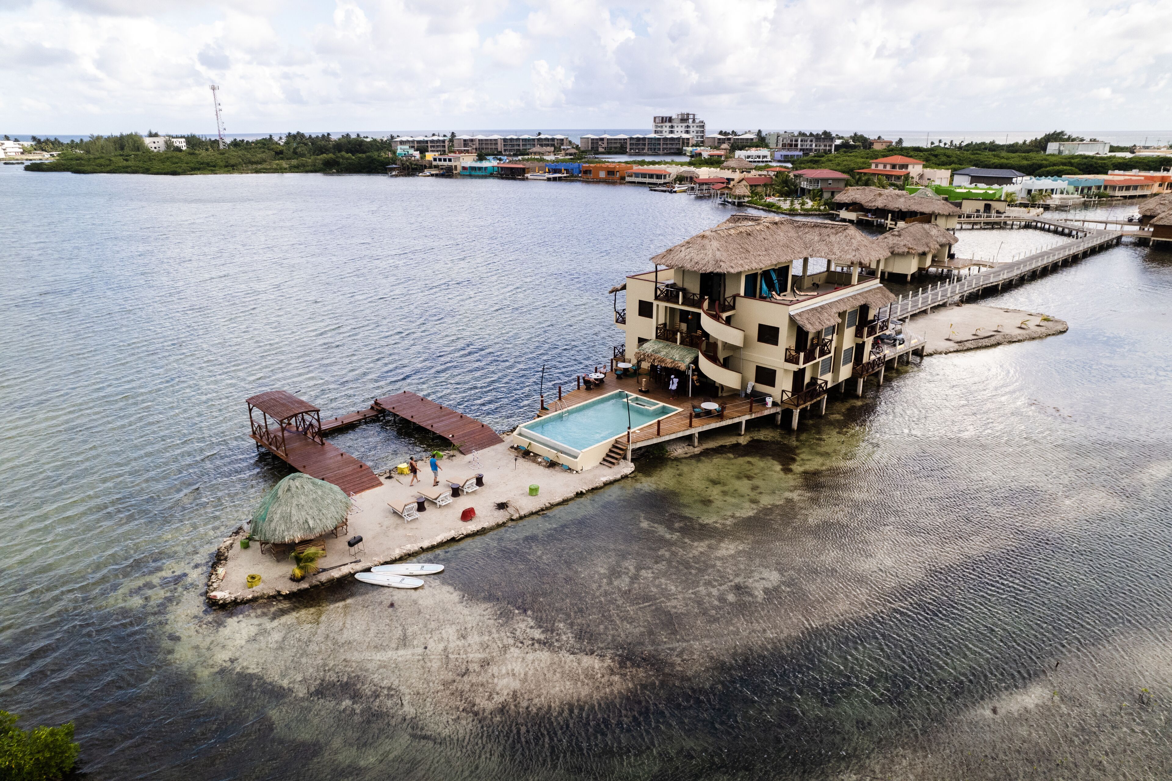 A waterfront property with a swimming pool, thatched-roof structures, and a dock extending into the water.