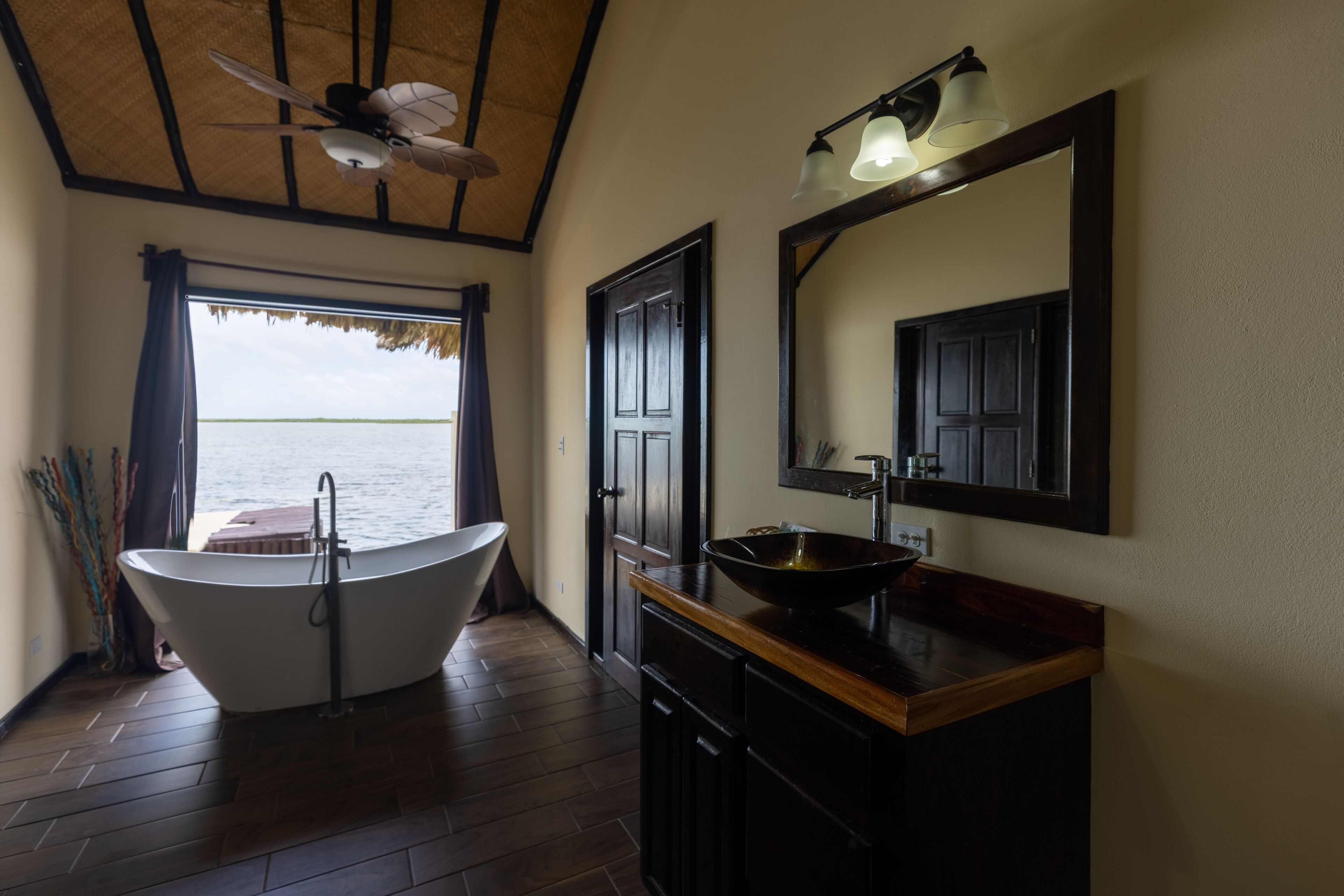 A bathroom with a freestanding bathtub, a wooden vanity with a bowl sink, a large mirror, and a ceiling fan.