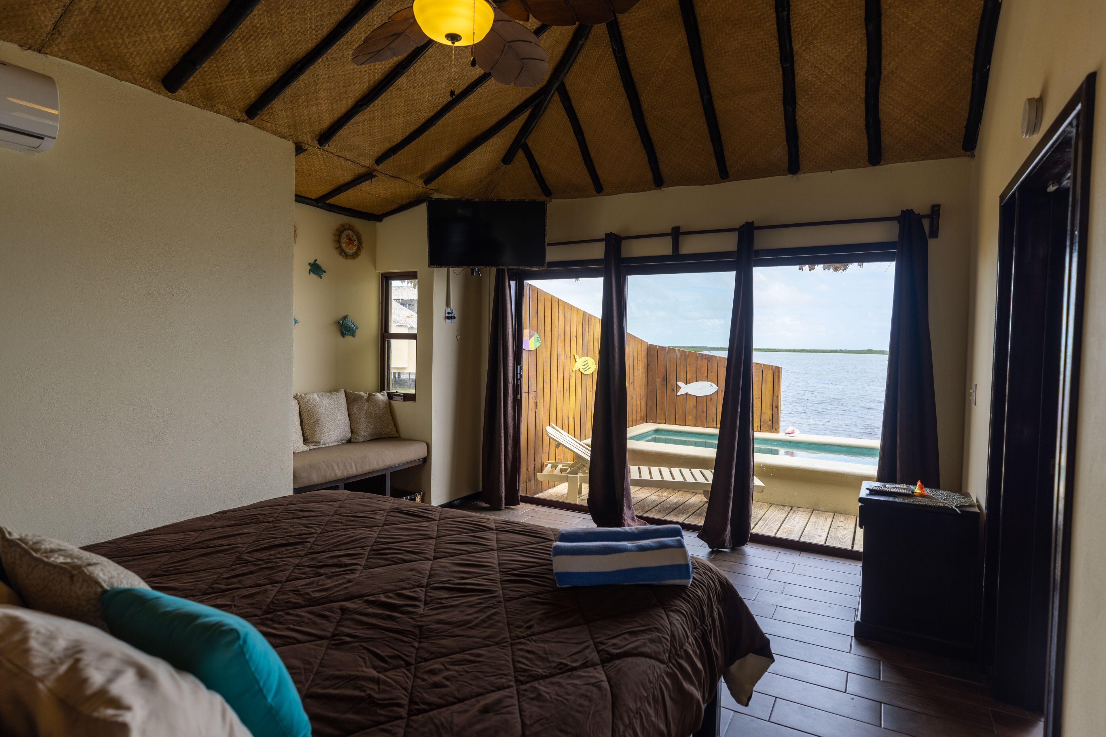 Un dormitorio con una cama grande, ventilador de techo, vista al océano y terraza de madera con hidromasaje.