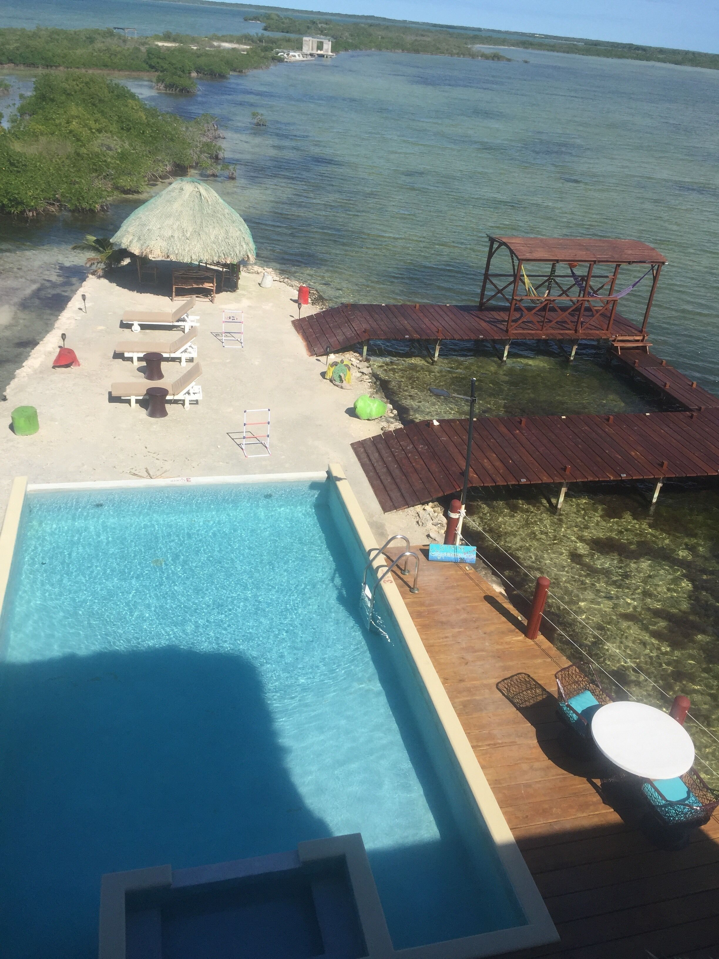 Un espace piscine doté de chaises longues, d’une structure à toit de chaume et d’une terrasse en bois qui s’avance sur l’eau.