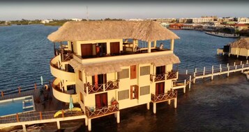 Een meerlaags overwater bungalow met rieten dak, balkons en een zwembad.