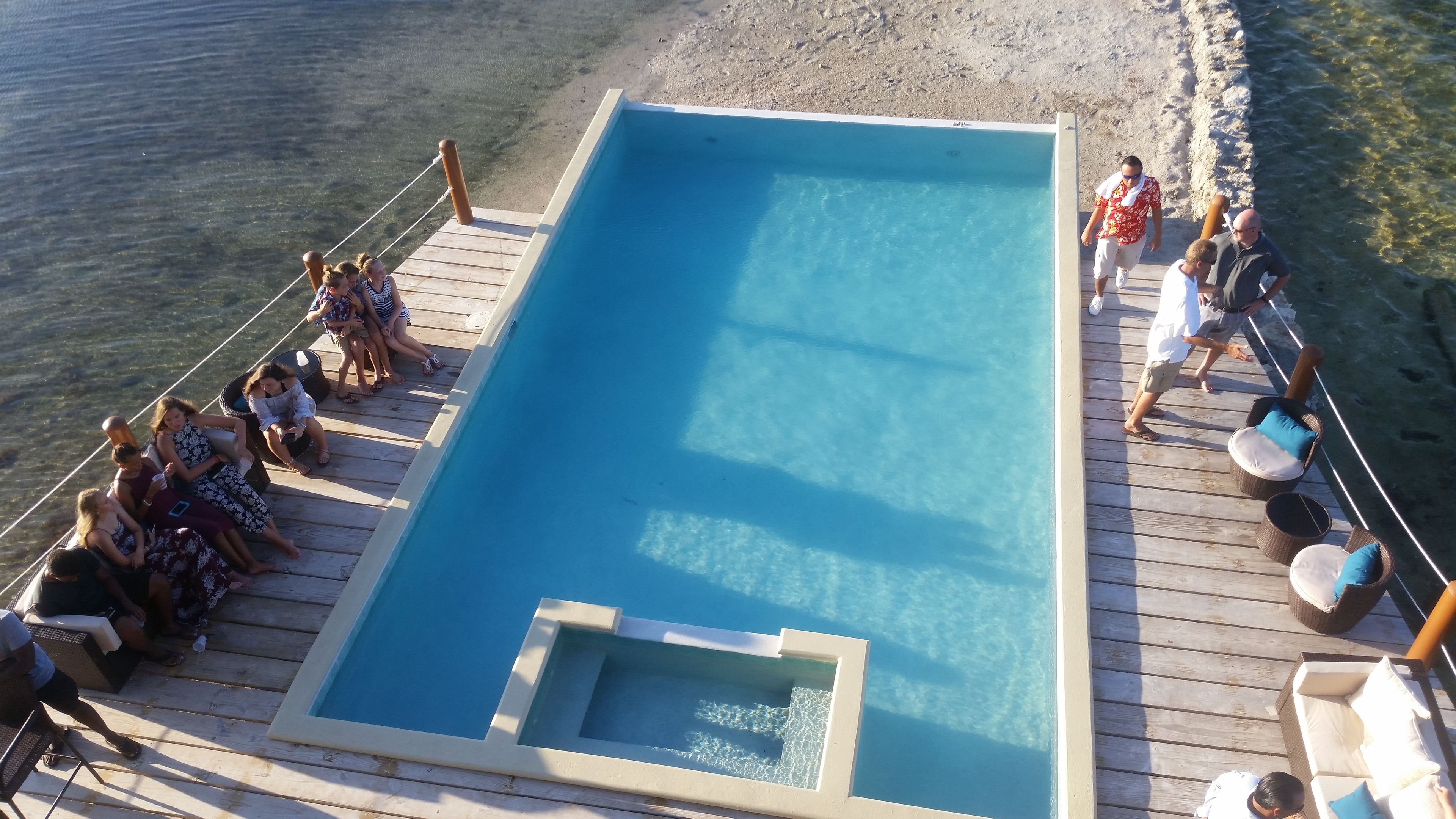 Une piscine rectangulaire sur une terrasse en bois, avec un petit jacuzzi au centre, entourée de chaises longues et délimitée par une barrière en corde.