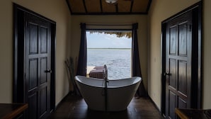 A hallway with a bathtub, wooden doors, and a view of a body of water. - Lina Point Belize Overwater Resort (San Pedro)