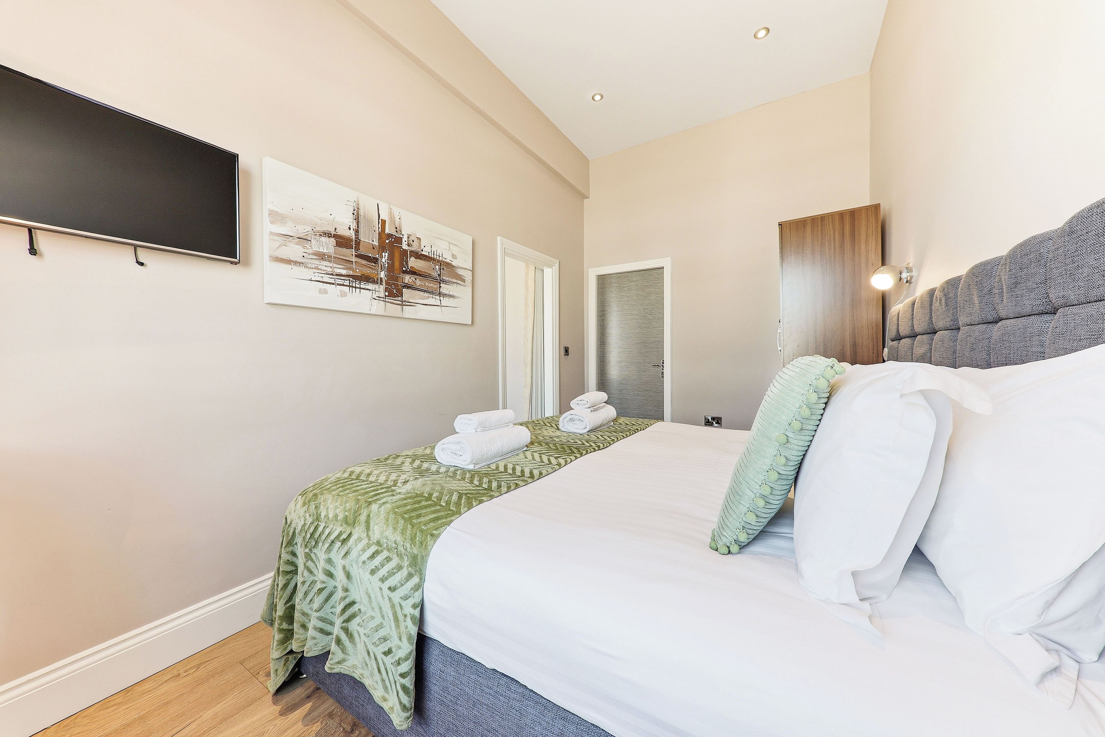 A hotel room with a bed, a painting, a door, and a wall-mounted light fixture.