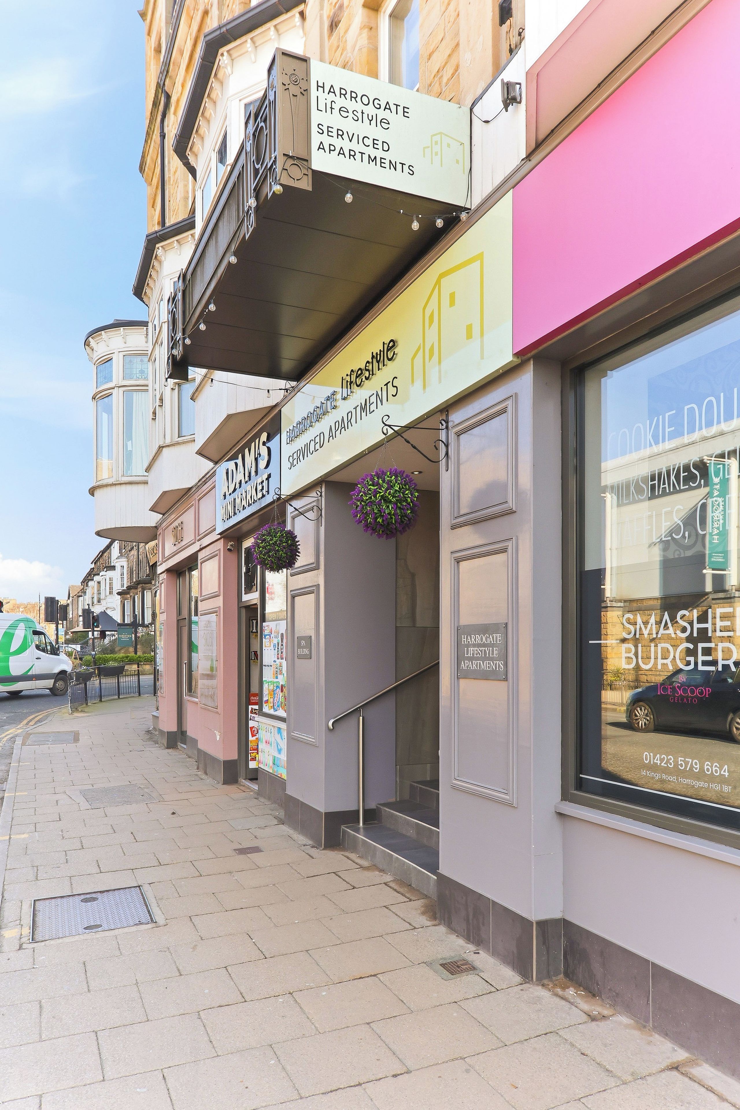 Vista de la calle con escaparates, incluyendo un letrero de Harrogate Lifestyle Apartments y una tienda de Cookie Dough Milkshakes, helados y gofres.